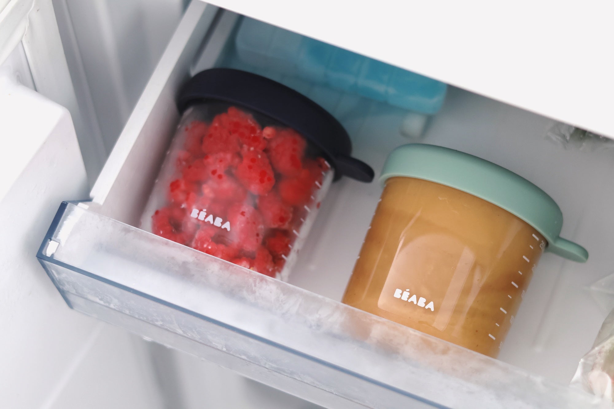 Two glass containers with red and brown food inside an open refrigerator.