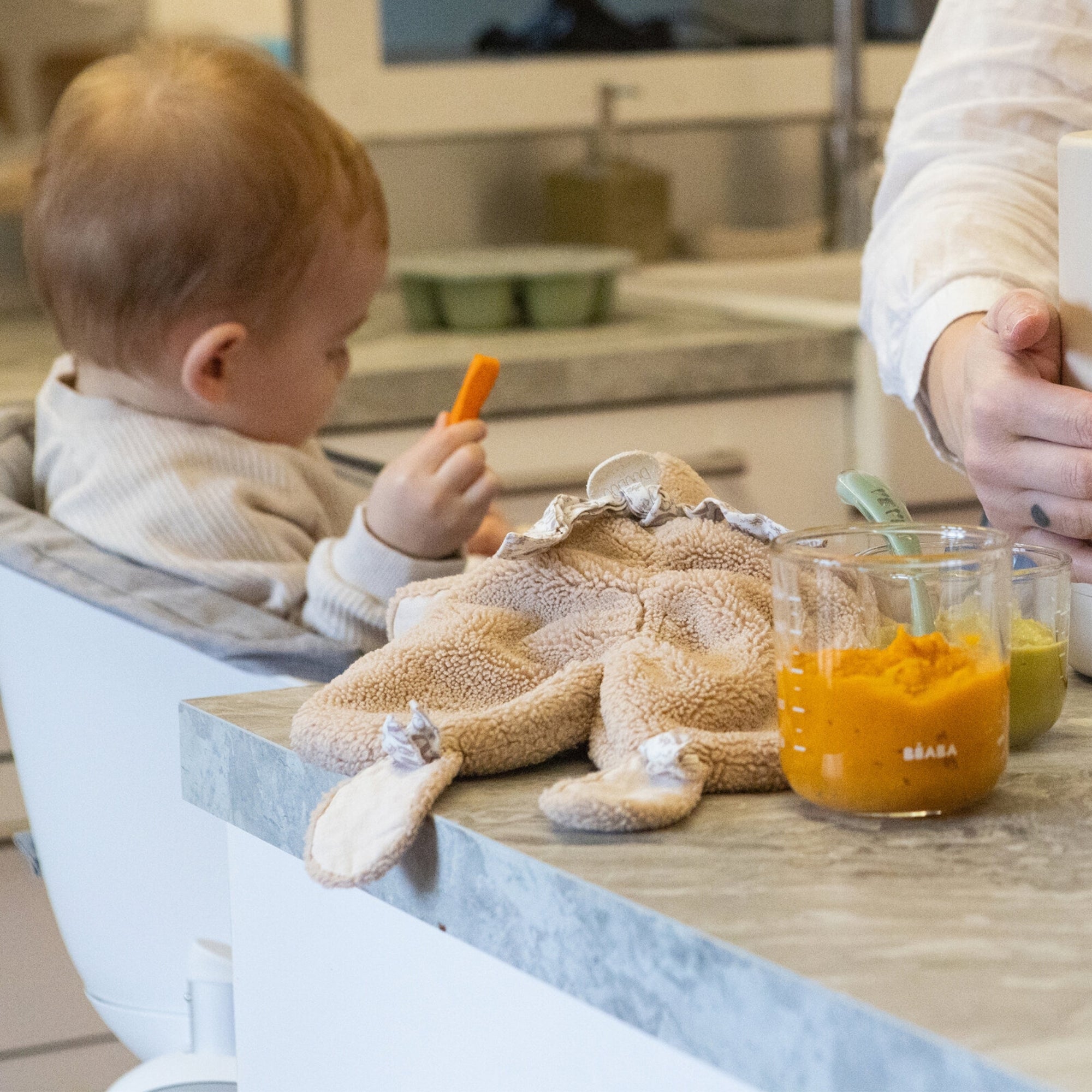 Baby sitting in a high chair holding a carrot 